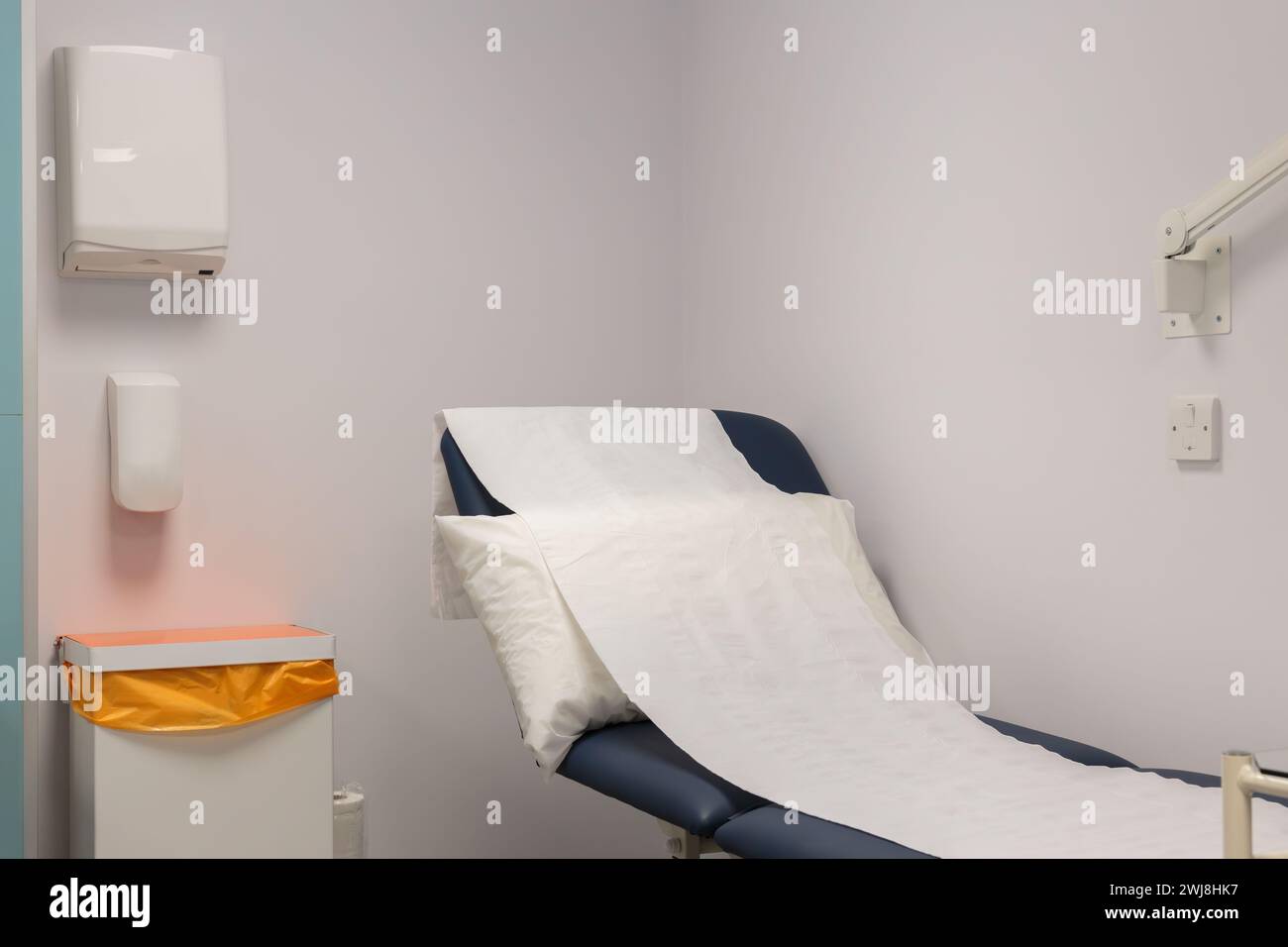 Un divano medico interno rialzato, che mostra l'attenzione sul cuscino bianco e rotolo del letto di carta con dispenser a parete semplice e contenitore per rifiuti. Foto Stock