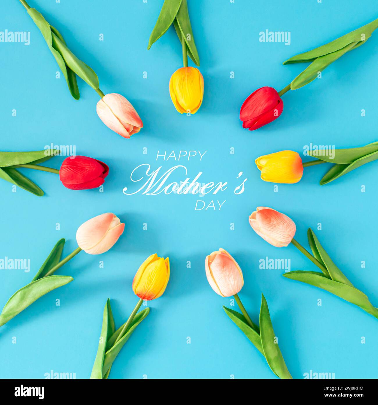 Composizione creativa primaverile realizzata con fiori di tulipani colorati con testo "Happy Mother's Day" su sfondo blu. Concetto minimalista per la giornata della mamma. Foto Stock