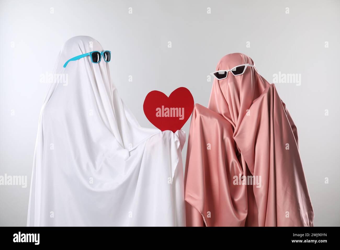 Fantasmi carini. Abbinalo a lenzuola e occhiali da sole a colori con cuore rosso su sfondo grigio chiaro Foto Stock