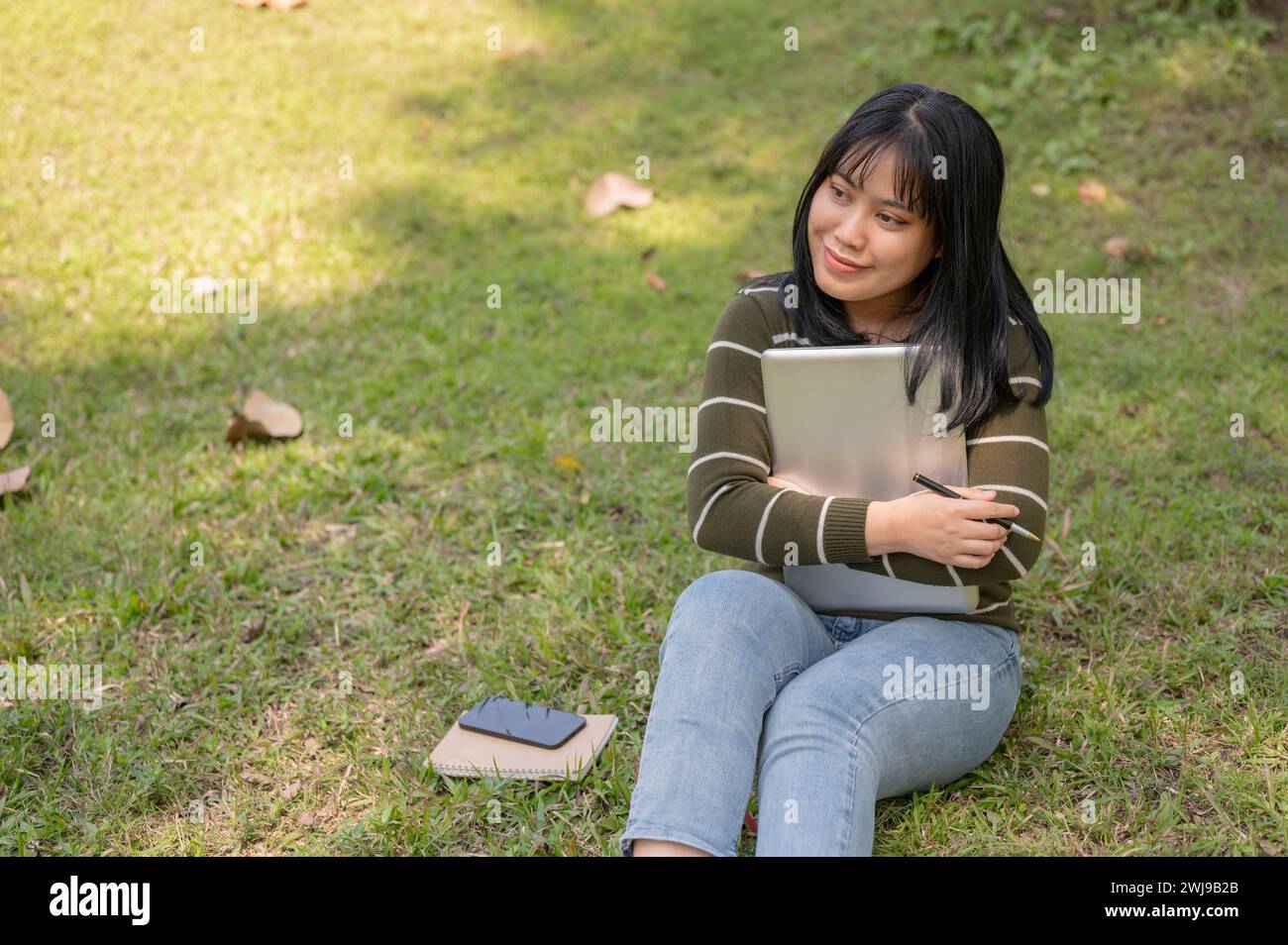Una bella studentessa asiatica del college è seduta sull'erba in un parco universitario con il suo portatile. Foto Stock