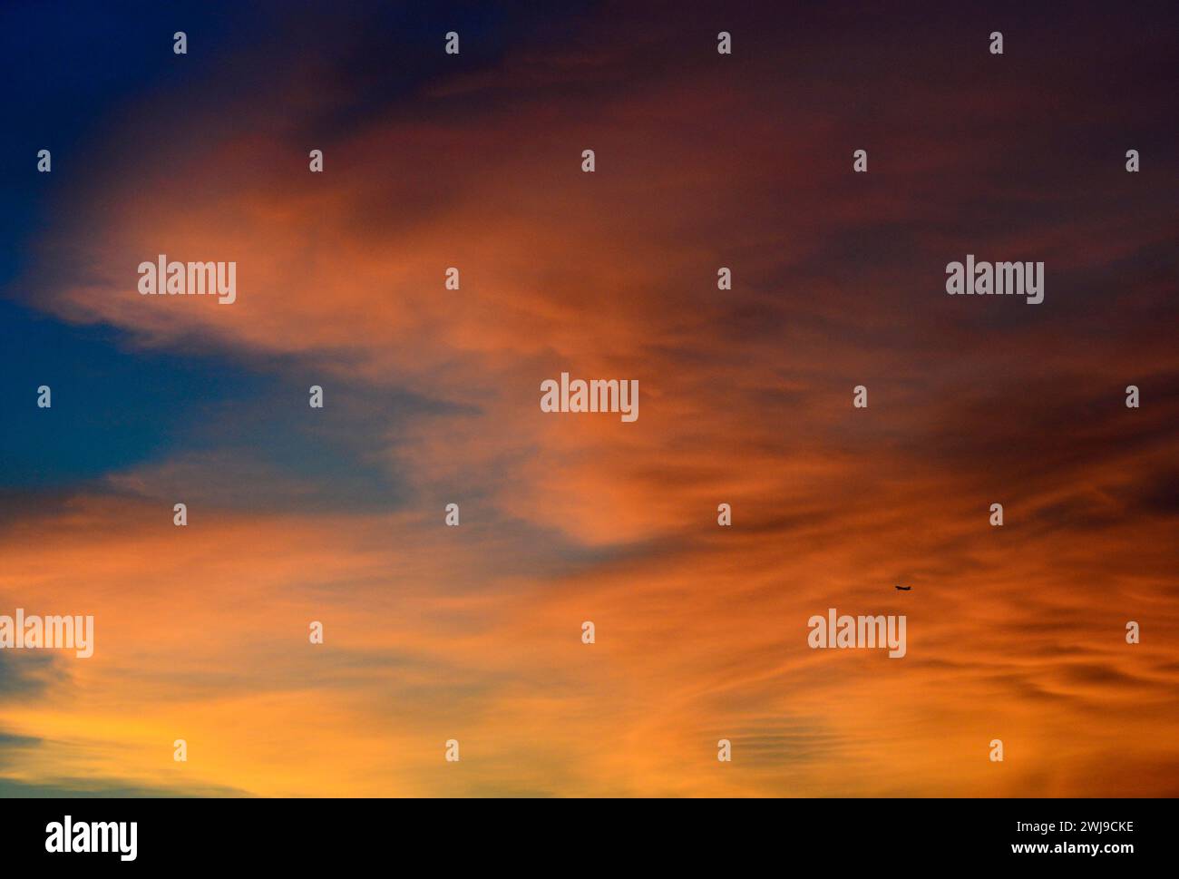 Un aereo che vola sotto le nuvole arancioni durante il tramonto a Hong Kong. Foto Stock