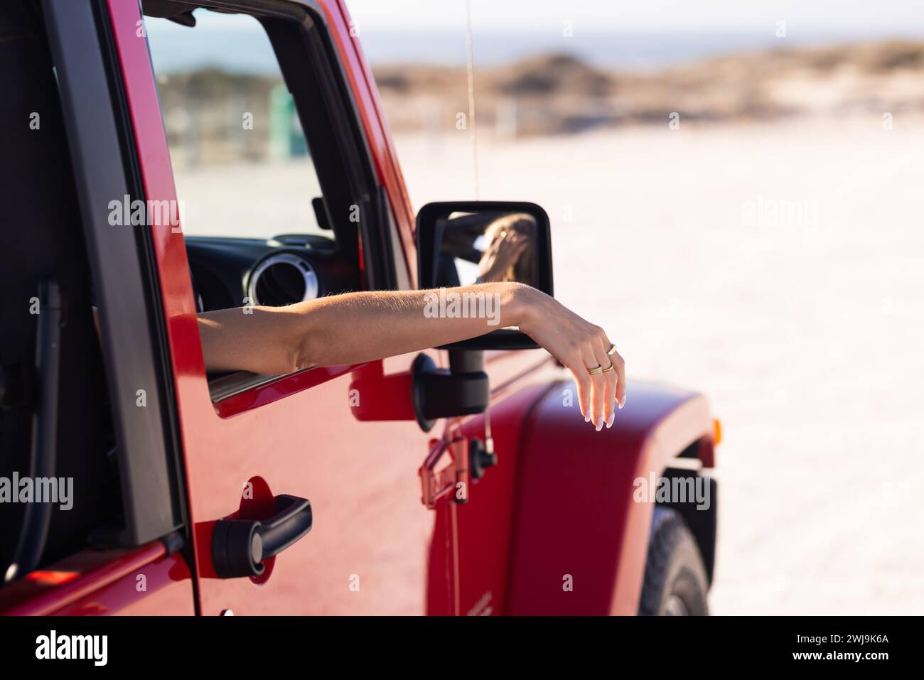 Una persona distende il braccio dal finestrino di un veicolo rosso durante un viaggio in auto, all'aperto Foto Stock