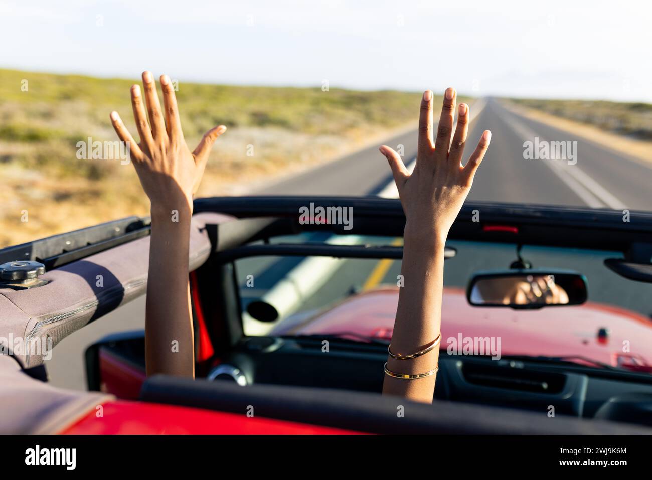 Alzate le mani di gioia durante un giro in auto con capote in una giornata di sole durante un viaggio su strada Foto Stock