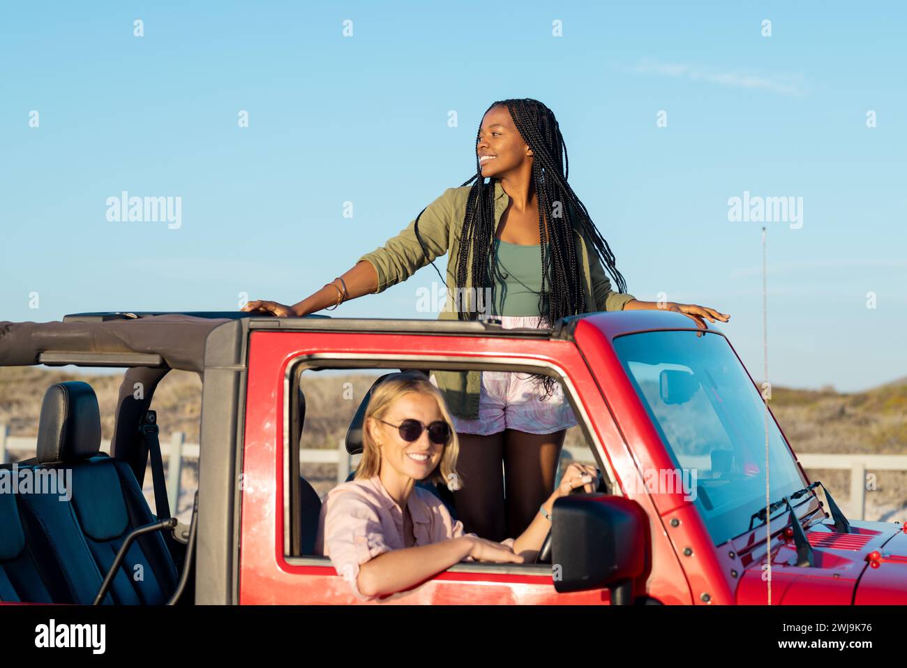 Due donne condividono gioia in un viaggio di sole su una jeep rossa. Foto Stock