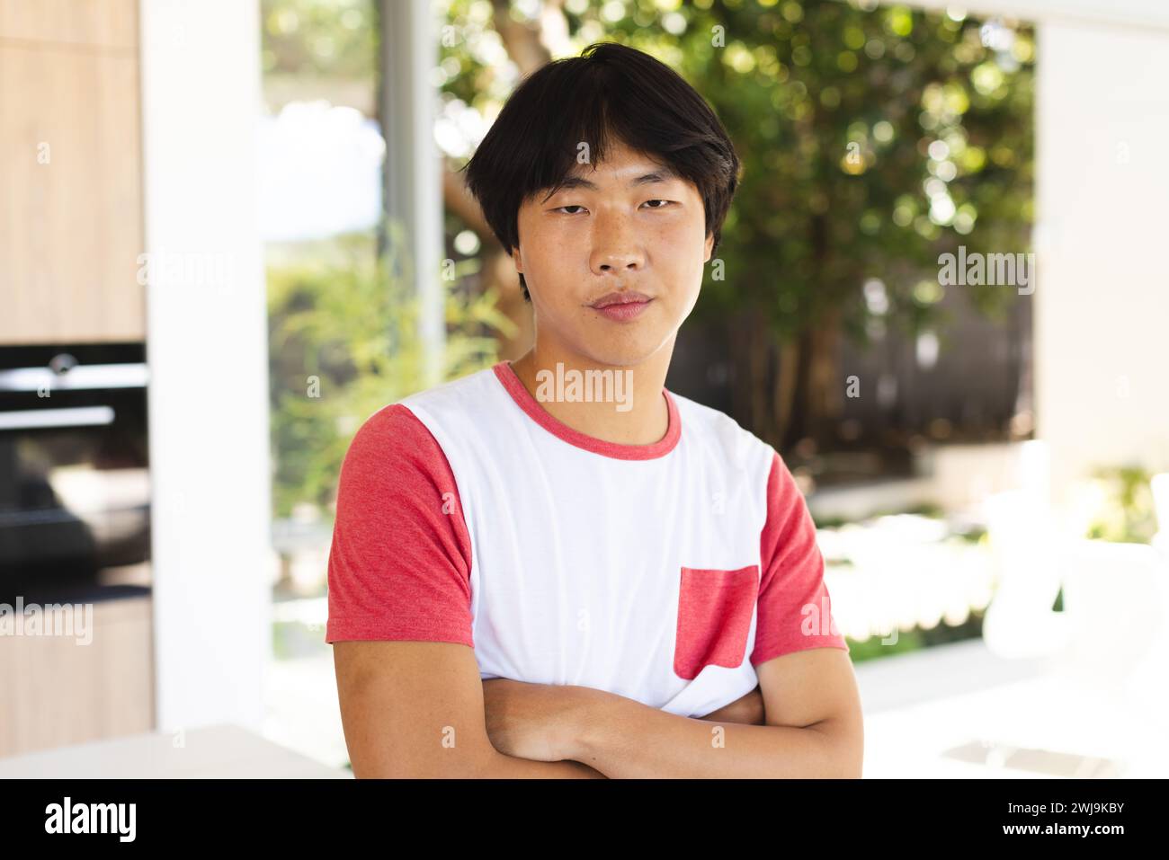 Adolescente ragazzo asiatico sta con fiducia a casa, le braccia incrociate Foto Stock