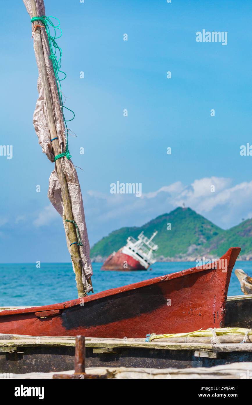 Una tradizionale barca da pesca rossa anticipa una nave a terra al largo della costa di Bahia Santana, mostrando il contrasto tra la pesca su piccola scala e il mar Foto Stock