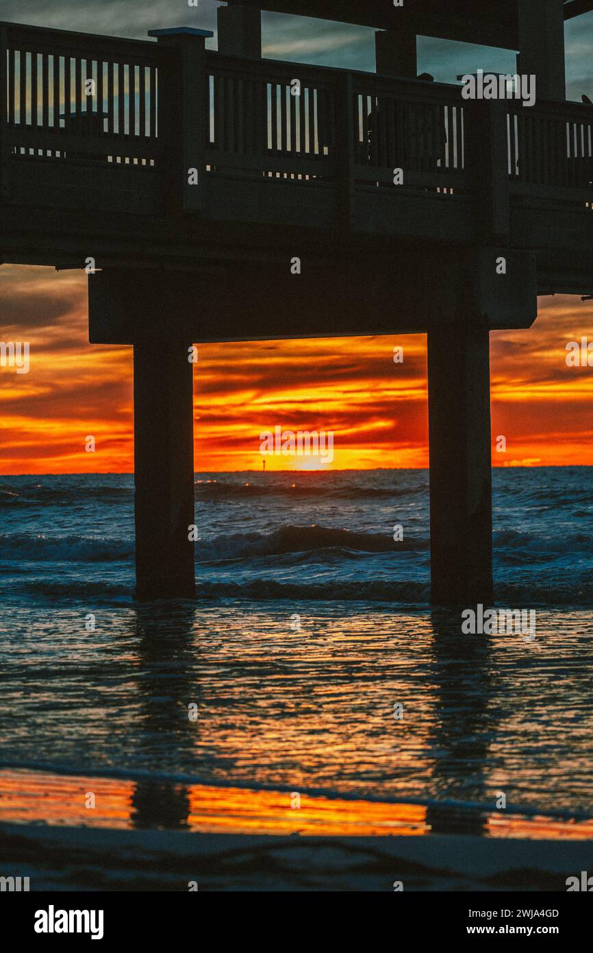 Una vista mozzafiato di un tramonto vibrante con sfumature ardenti che si riflettono sull'acqua sotto un molo su una spiaggia di Miami, Florida. Foto Stock