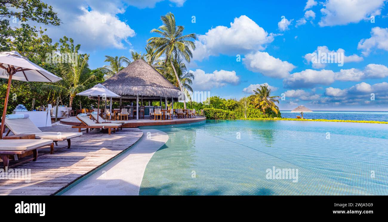 Panorama mozzafiato, piscina, cielo azzurro e soleggiato. Hotel resort tropicale alle Maldive. Tempo libero relax benessere vibrazioni tranquille, sedie, lettini e ombrelloni Foto Stock