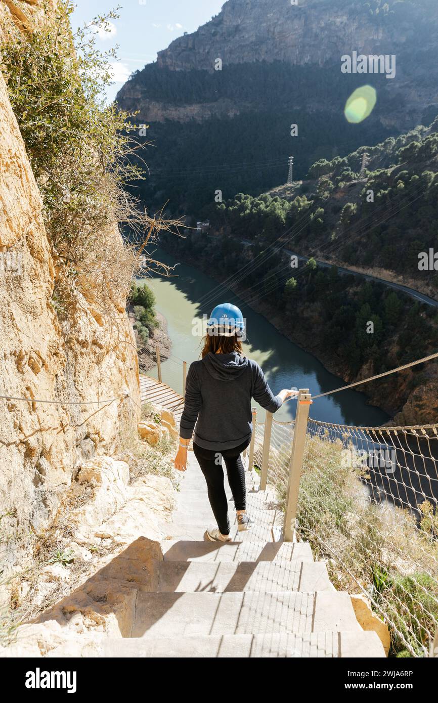 Escursionista anonimo che scende una scala sul sentiero del Caminito del Rey con un fiume e montagne sullo sfondo Foto Stock