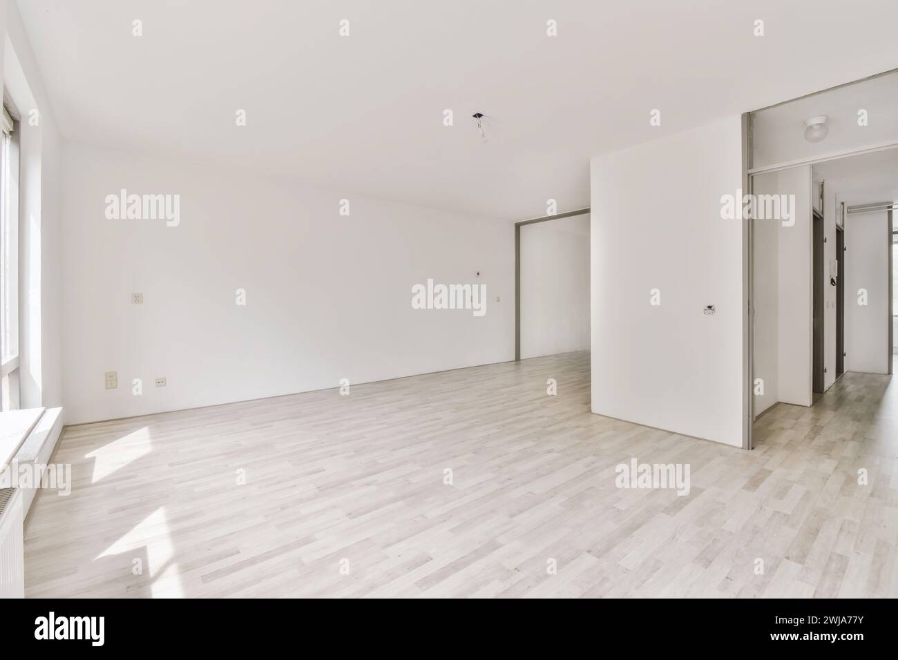 Una sala vuota luminosa e ariosa con pavimento in laminato di legno chiaro e pareti bianche, con luce del sole che scorre dentro Foto Stock
