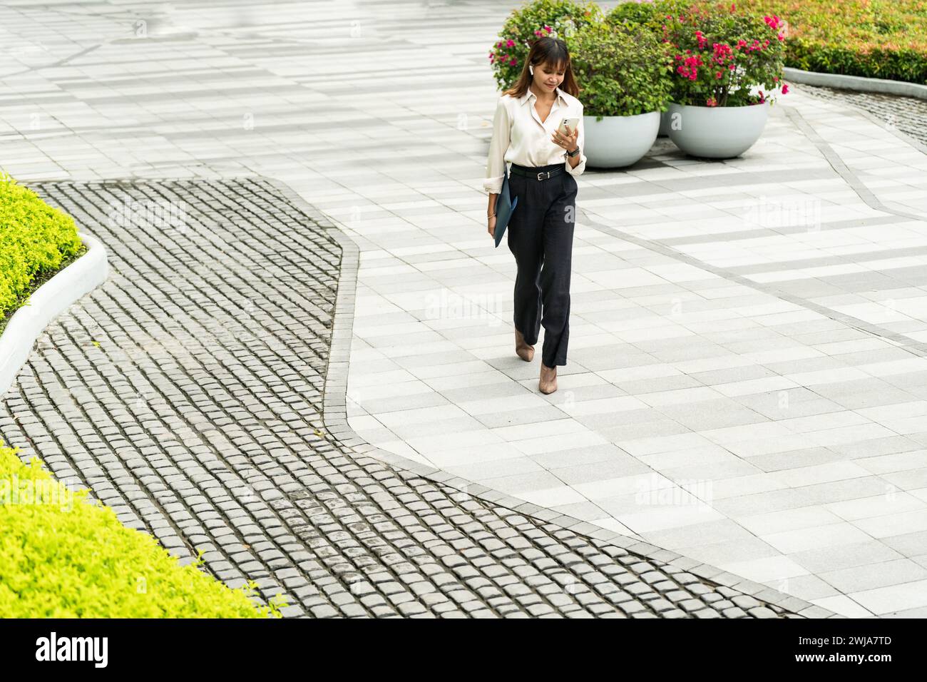 Una donna d'affari asiatica è concentrata nel suo telefono mentre cammina lungo un sentiero nella città di Chiang mai. Foto Stock