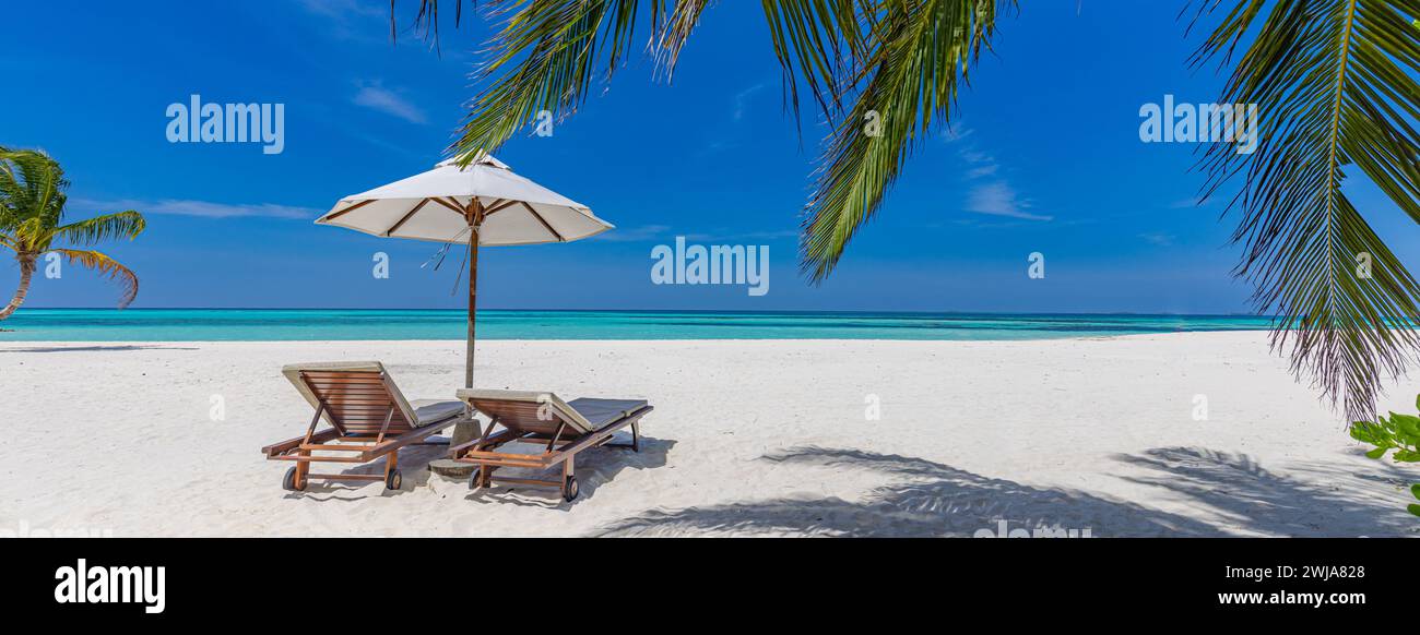 Bellissimo cielo panoramico di sabbia marina. Relax tropicale, spiaggia di lusso, soleggiato paesaggio estivo dell'isola. Amore coppia sedie ombrello palma lascia romantica costa Foto Stock