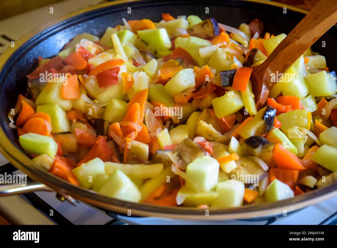 Processo di cottura della salta a casa. Verdure stufate e cucchiaio di legno nella padella. Ingredienti misti cipolle, carote, zucchine, melanzane, peperone Foto Stock