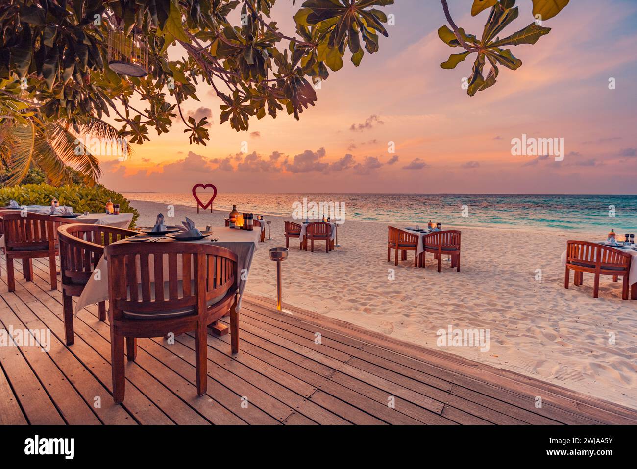 Ristorante all'aperto sulla spiaggia. Tavolo al ristorante sulla spiaggia tropicale. Candele luminose a LED, tavoli in legno e sedie sotto il bellissimo cielo del tramonto Foto Stock