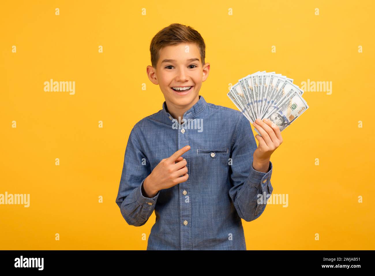 Allegro ragazzo adolescente in camicia in denim che punta a un fan di banconote da un dollaro Foto Stock