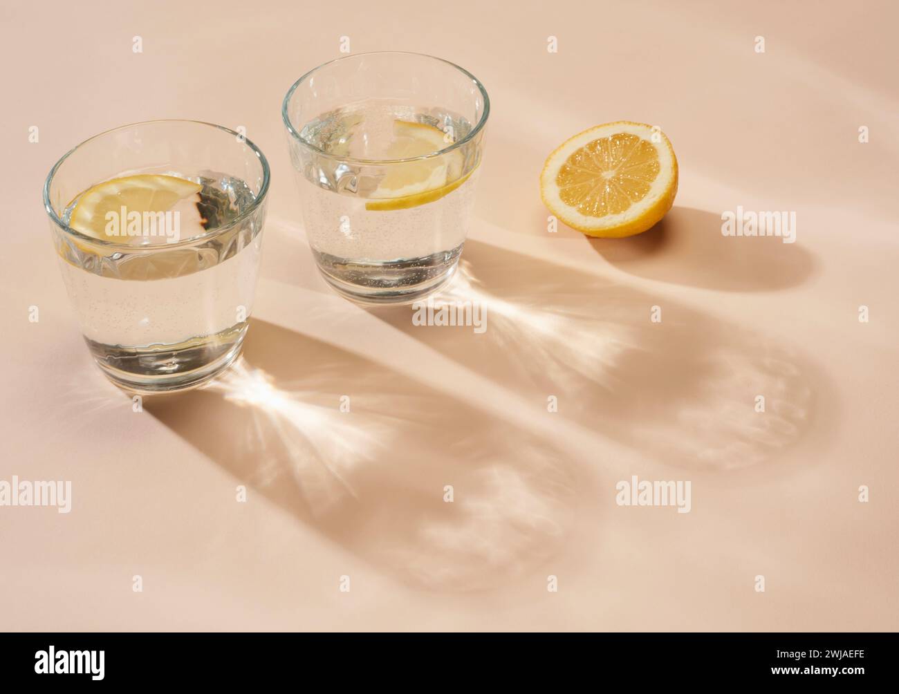 Bicchieri d'acqua con limone a fette su sfondo color crema, con ombre Foto Stock