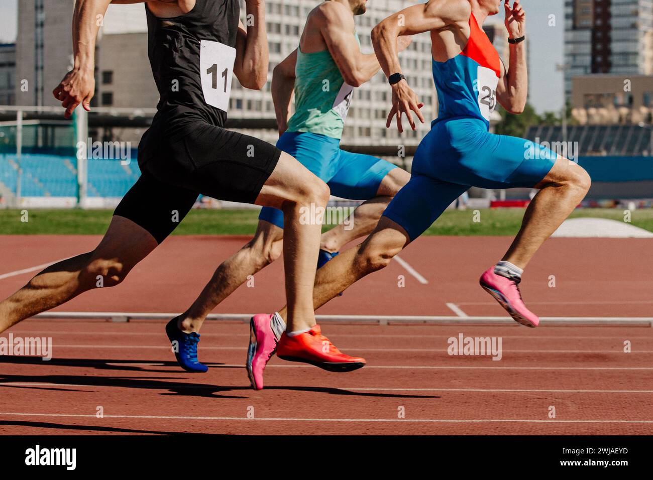 tre atleti maschi che corrono su pista rossa, i muscoli sono tesi, gareggiano ferocemente Foto Stock