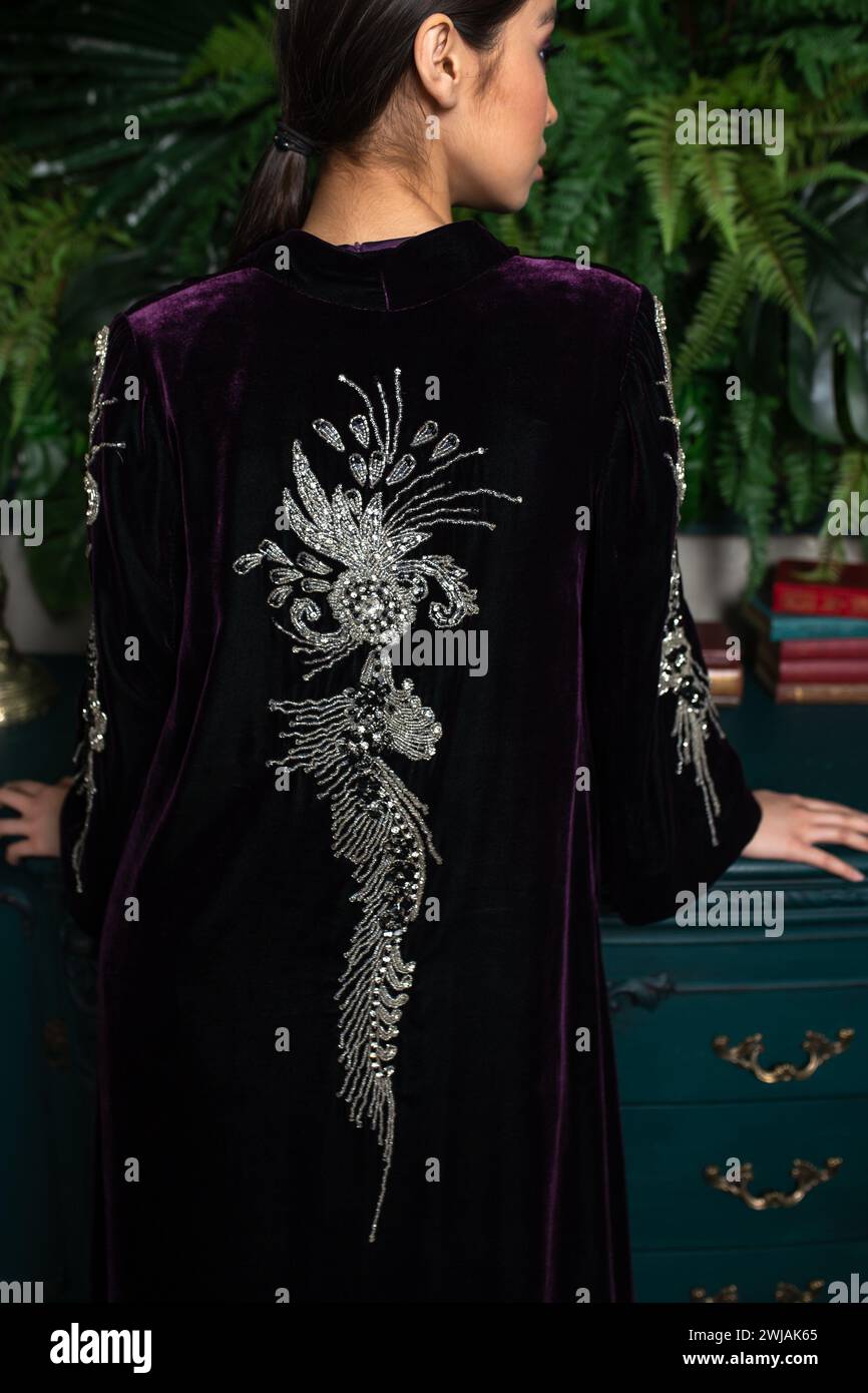 Modello giovane in velluto viola con ricami argentati su uno sfondo verde lussureggiante. Riprese in studio con illuminazione controllata e colori vivaci. IO Foto Stock