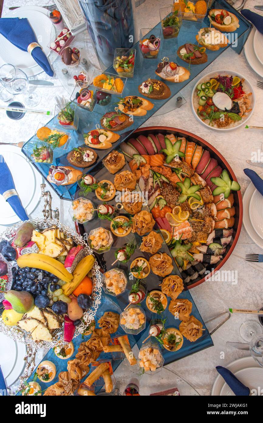 Un sontuoso buffet che offre un ricco assortimento di pesce fresco, sushi, insalate, frutta e pasticcini, splendidamente disposto su un tavolo bianco immacolato Foto Stock
