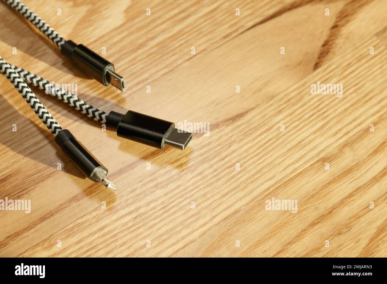 Tre tipi di connettore per cavo 3 in 1 per caricabatterie telefonico su una scrivania in legno Foto Stock