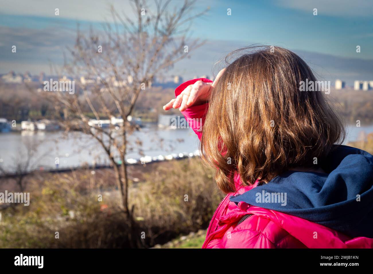 Una donna irriconoscibile alza la mano per coprire la luce del sole mentre guarda il paesaggio urbano, preso da dietro. Foto Stock