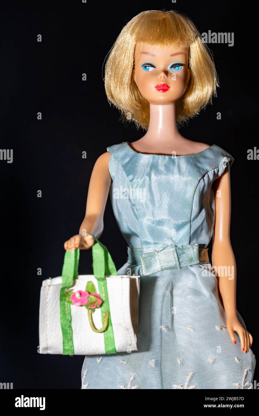 Una bambola Barbie degli anni '1960, contrassegnata con "copyright 1958, Made in Japan", indossa una guaina blu satinata con una borsa bianca su sfondo scuro Foto Stock
