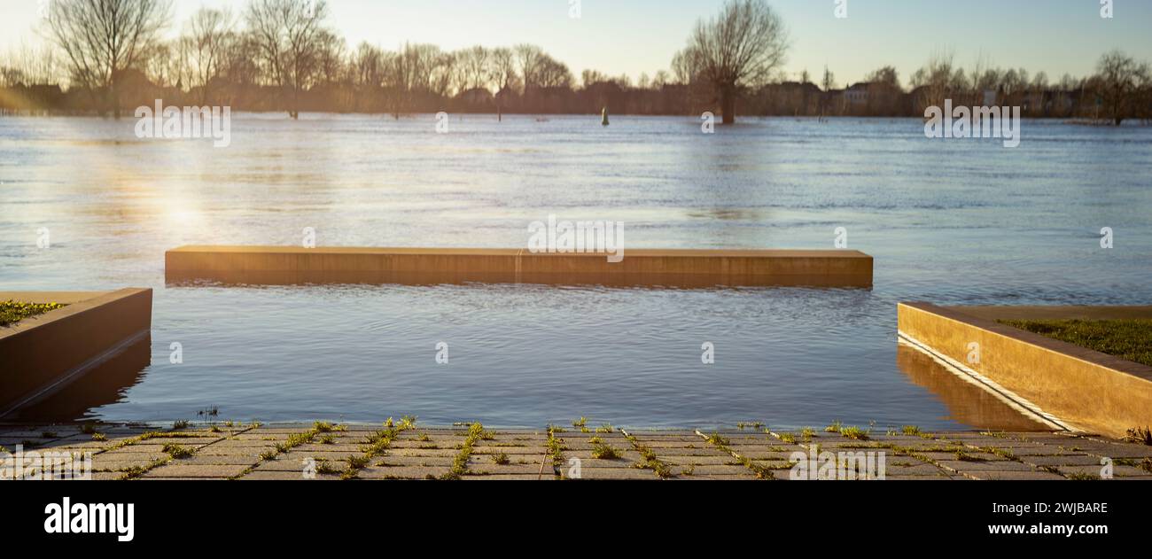 Vista super grandangolare della panchina sul bordo dell'alto livello dell'acqua del fiume IJssel, viale della città torre di Zutphen con ponte in acciaio sullo sfondo Foto Stock