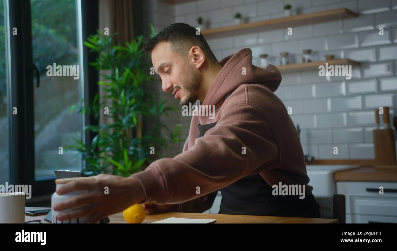 Vlogger uomo in un grembiule che parla con una webcam per tablet, registra video su come fare limonata nella cucina moderna di casa. Trasmissione online, amico le Foto Stock