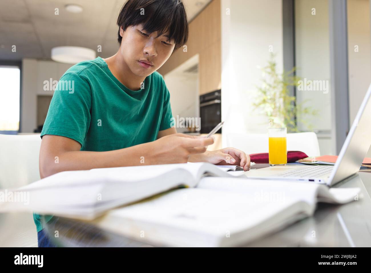 Adolescente ragazzo asiatico studia intensamente a casa, circondato da libri Foto Stock