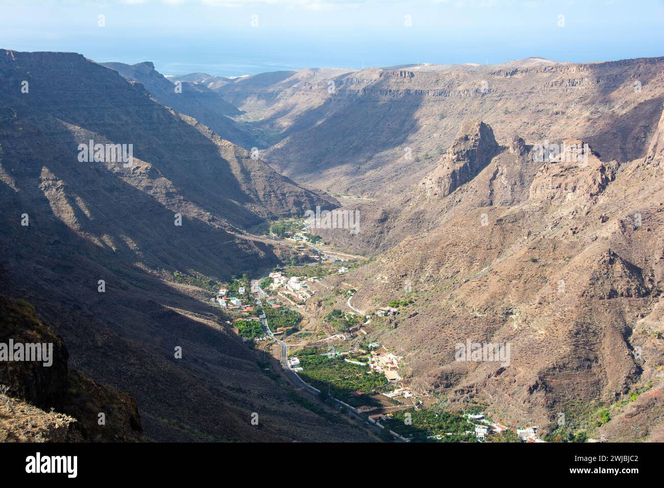 Montagne con un piccolo villaggio nella valle sull'isola Canaria di Gran Canaria in Spagna, con cielo blu e nuvole Foto Stock