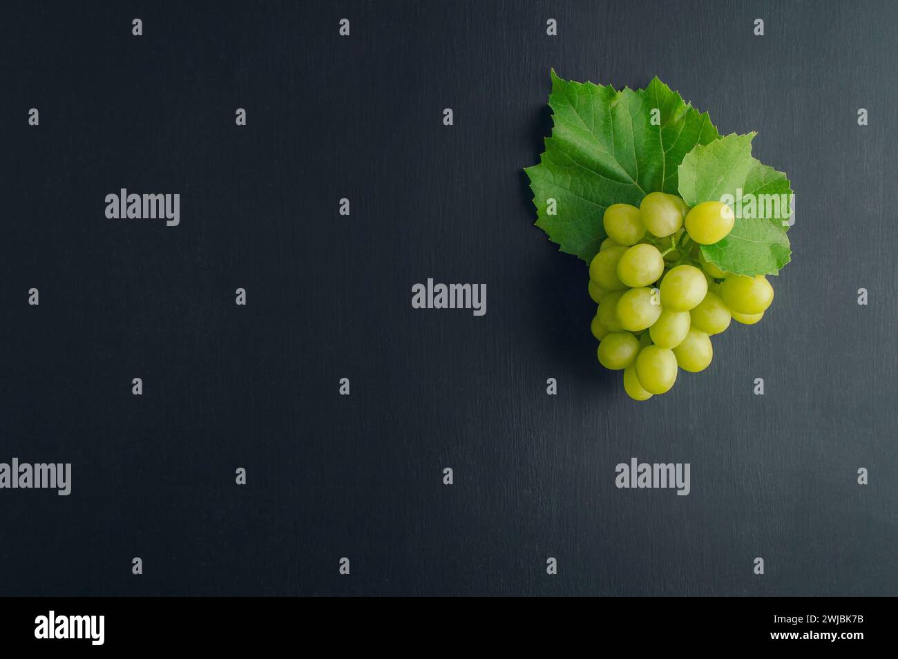 Un mucchio d'uva. Concetto di agricoltura e vinificazione. grappoli di uva con foglie su sfondo rustico scuro. La composizione del vino è piatta su un tavolo nero. Foto Stock