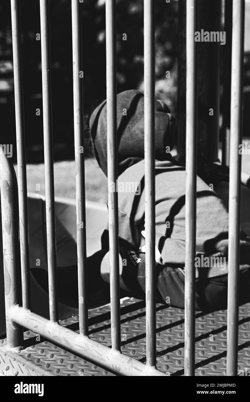 Una persona sdraiata su una panchina accanto a un cancello Foto Stock