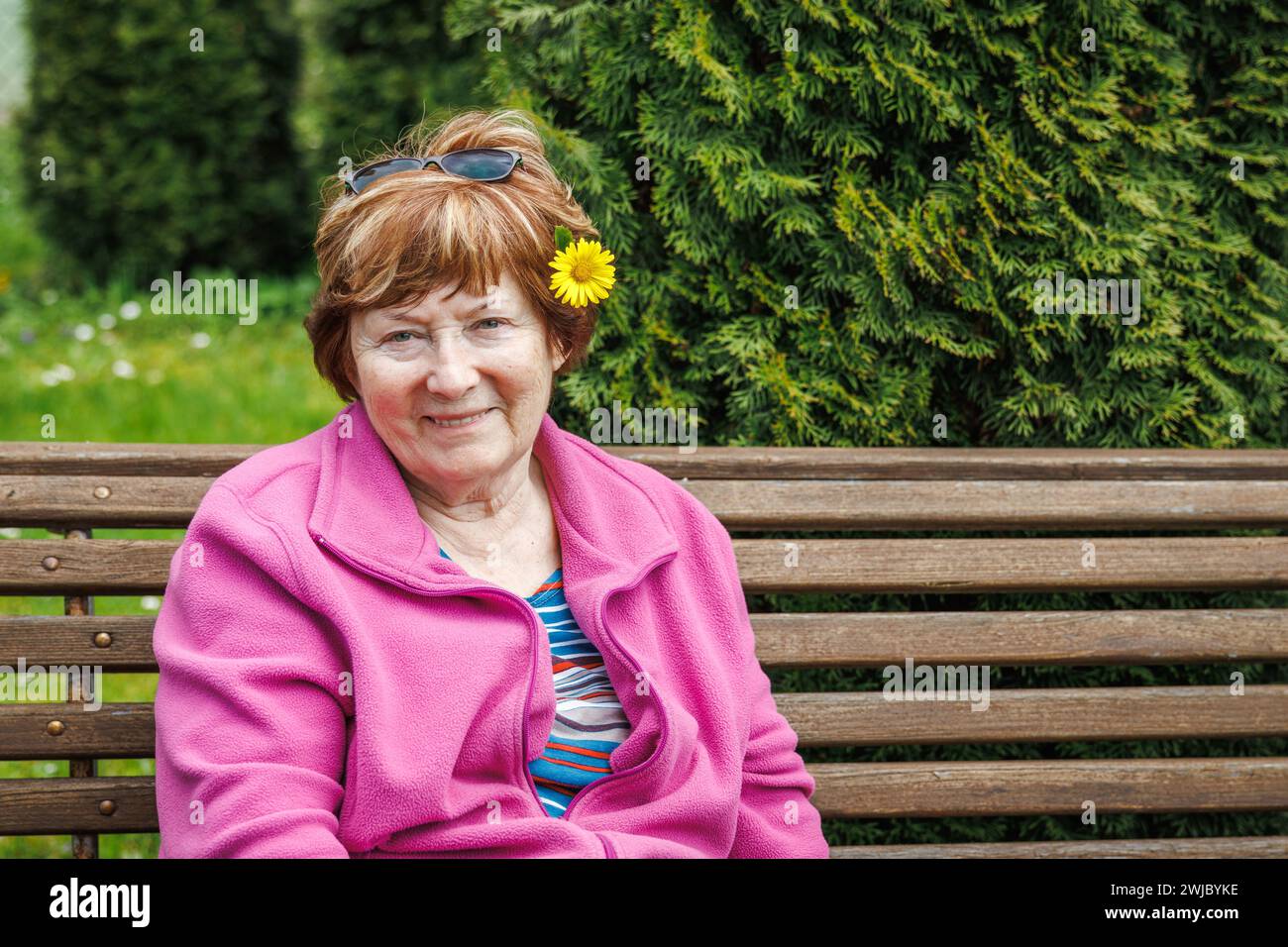 Ritratto di una donna anziana felice sorridente si rilassa sulla panchina in giardino in primavera. Goditi la splendida giornata primaverile Foto Stock