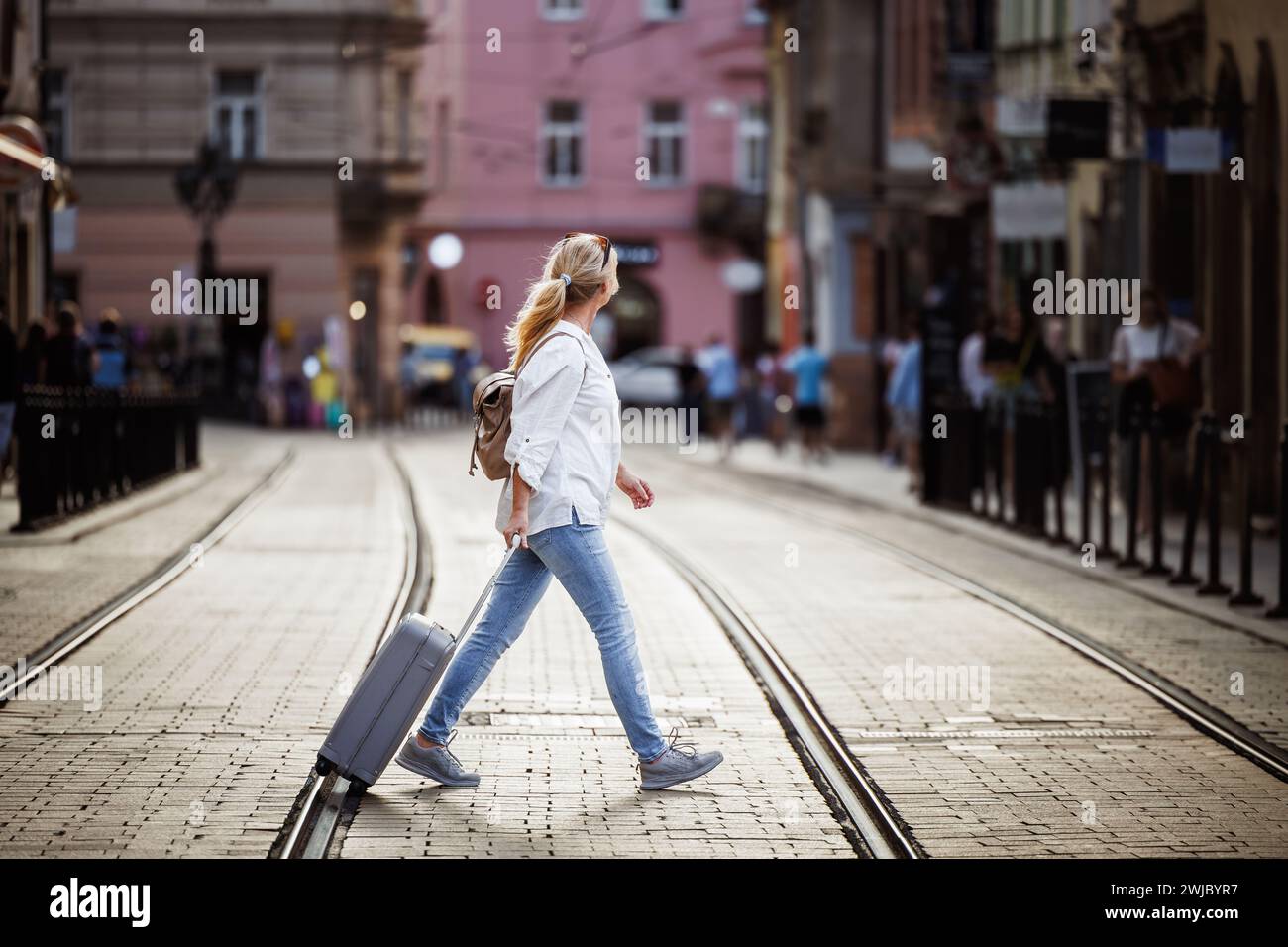 Una donna turistica con le valigie che cammina dall'altra parte della strada. Viaggi sicuri con un'assicurazione di viaggio affidabile Foto Stock