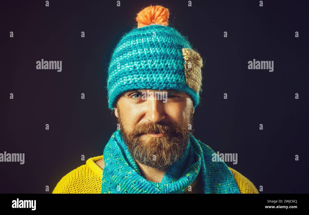 Ritratto ravvicinato di un uomo sorridente con barba in cappello e sciarpa. Accessori invernali. Bell'uomo barbuto in maglione giallo, sciarpa blu e cappello Foto Stock