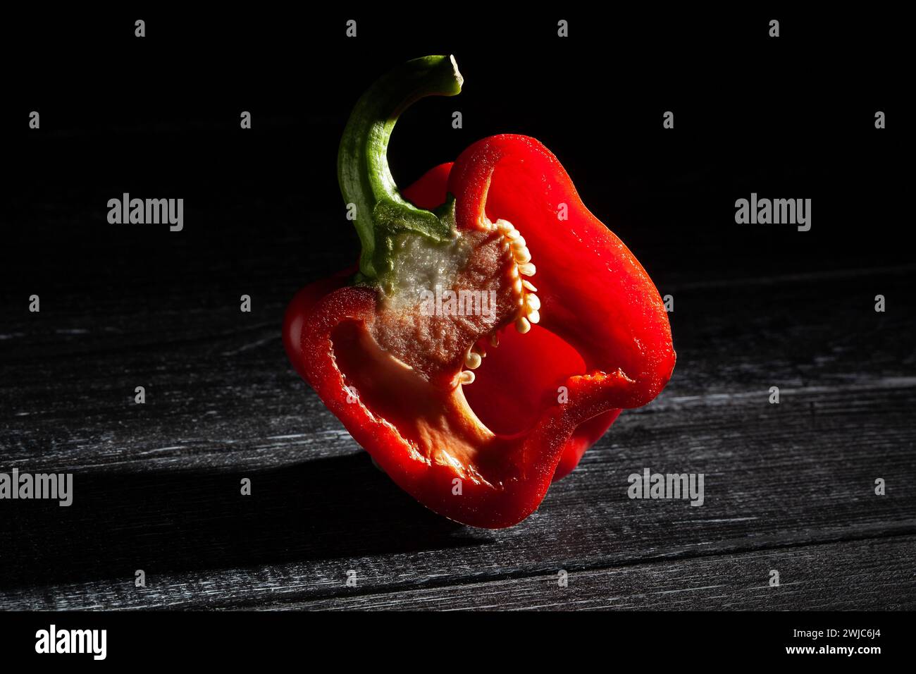 peperone rosso a fette su sfondo di legno nero Foto Stock