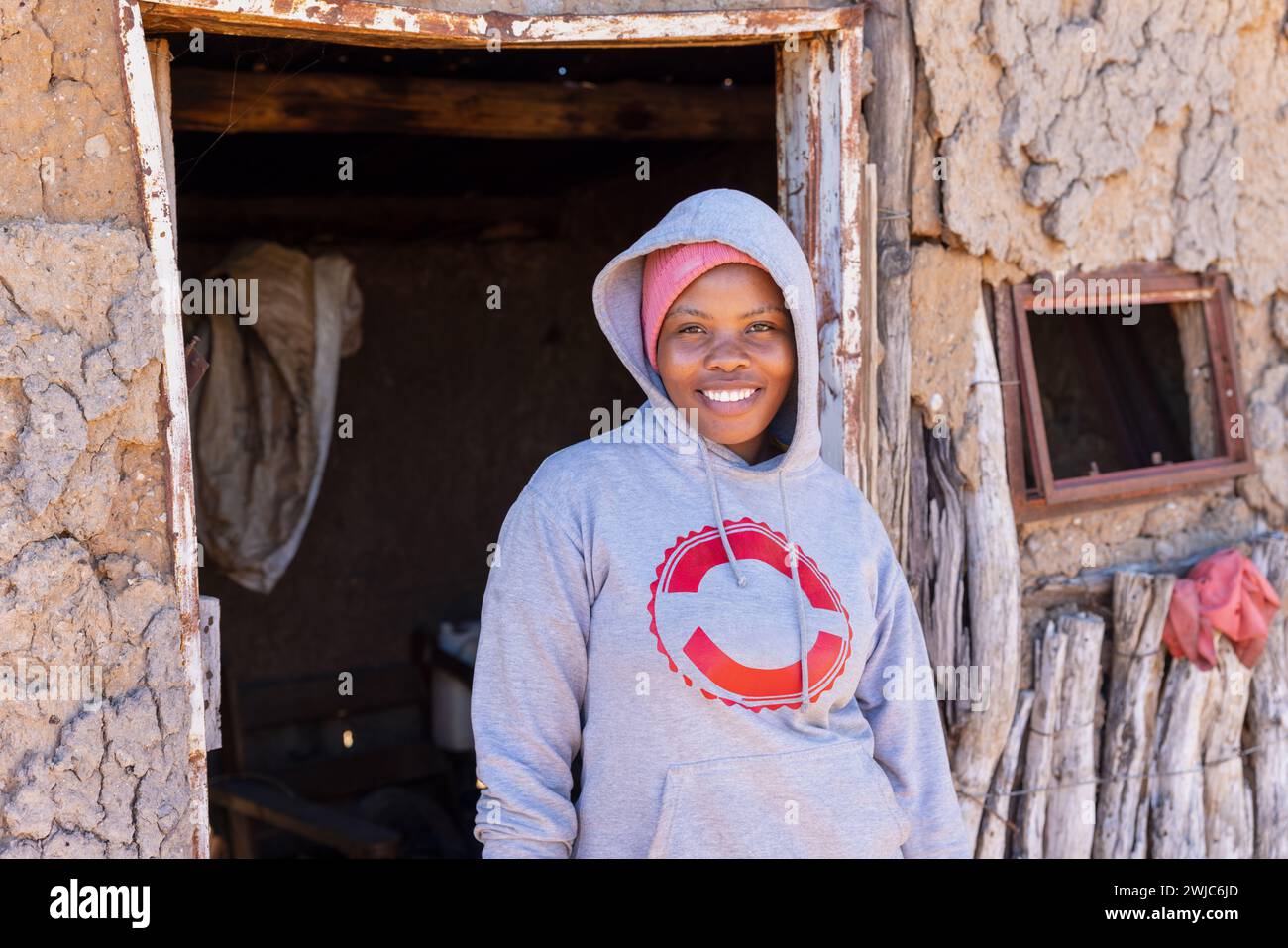 giovane donna africana nel villaggio, in piedi di fronte alle baracche della casa di fango Foto Stock