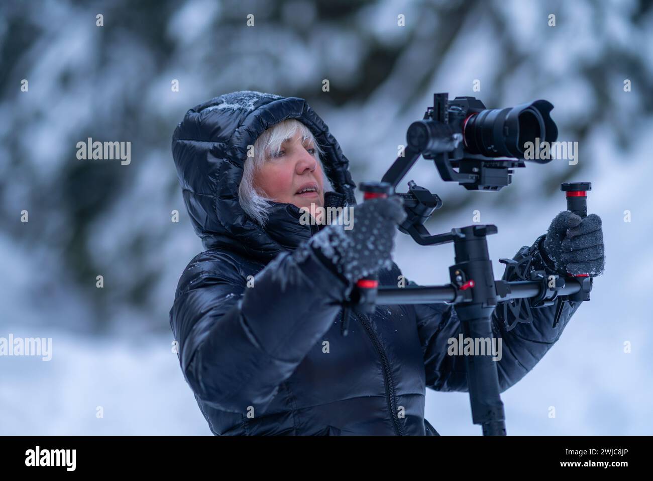 Una donna con giacca invernale tiene in mano una fotocamera con stabilizzatore con impugnatura a due mani Foto Stock