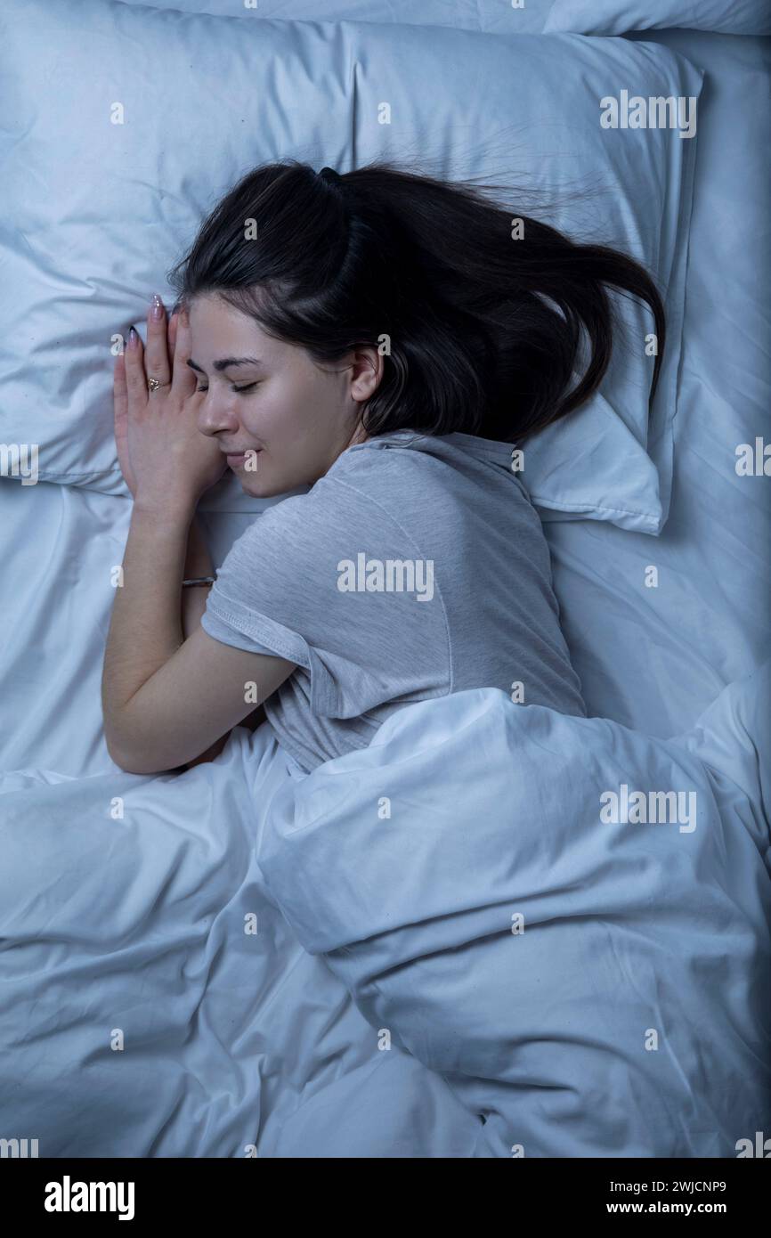 Una bella ragazza sta dormendo in un letto con un lenzuolo bianco. Foto Stock