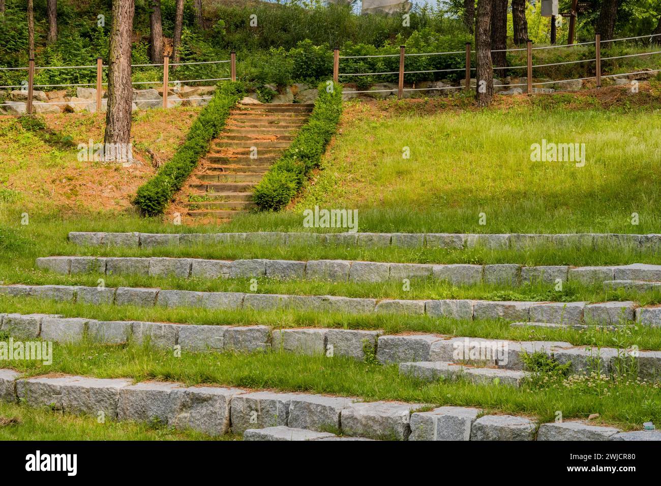 Posti a sedere nell'anfiteatro nel parco pubblico in blocchi di cemento con alberi e scalinata in legno sullo sfondo in Corea del Sud Foto Stock