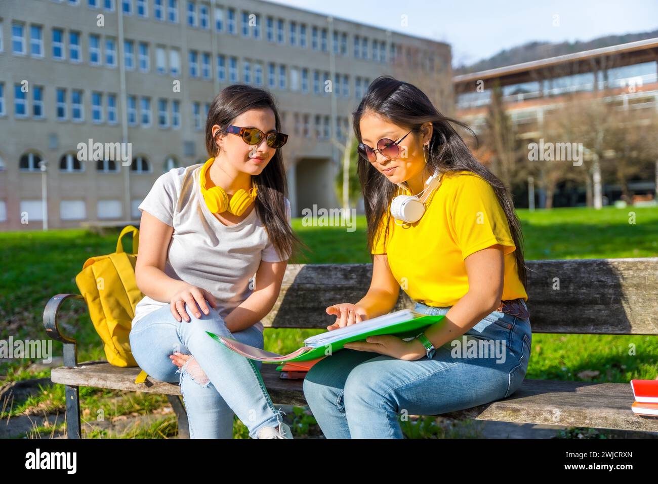 Studenti multietnici con cuffie che guardano i compiti seduti sulla panchina di un campus Foto Stock