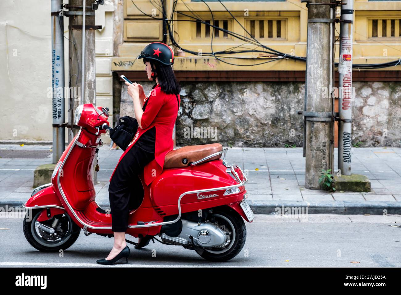 La giovane donna vietnamita si ferma per strada mentre guida una Vespa, per controllare il suo telefono cellulare. Hanoi, Vietnam. Foto Stock