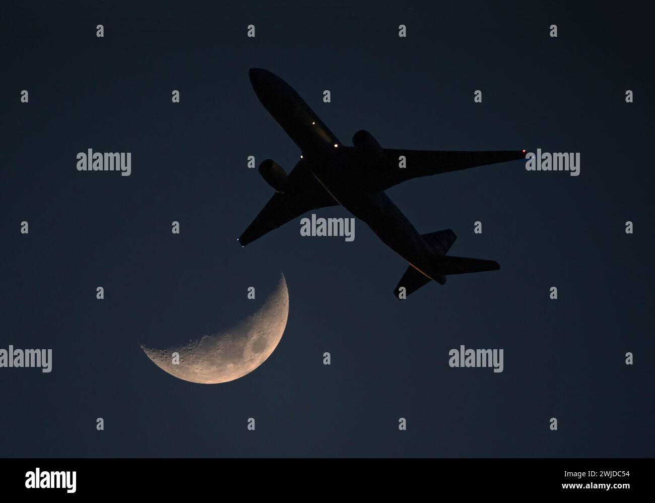 Un aereo di linea commerciale poco dopo il decollo passa da una luna crescente in un cielo blu profondo al crepuscolo. Foto Stock