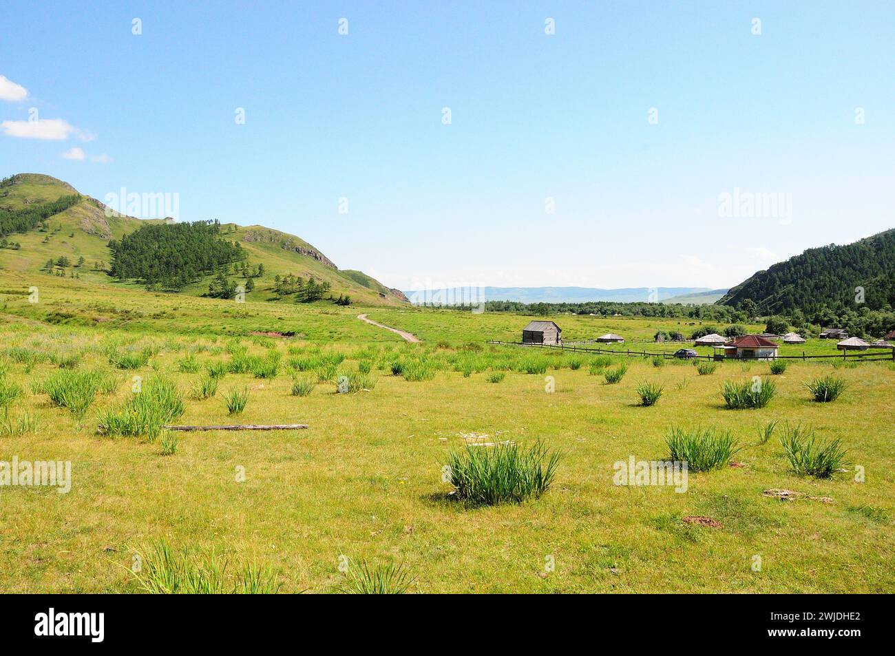 Una piccola fattoria con edifici tradizionali e una recinzione in legno in una pittoresca valle circondata da alte colline. Kazanovka, Khakassia, Siberia, Russia. Foto Stock