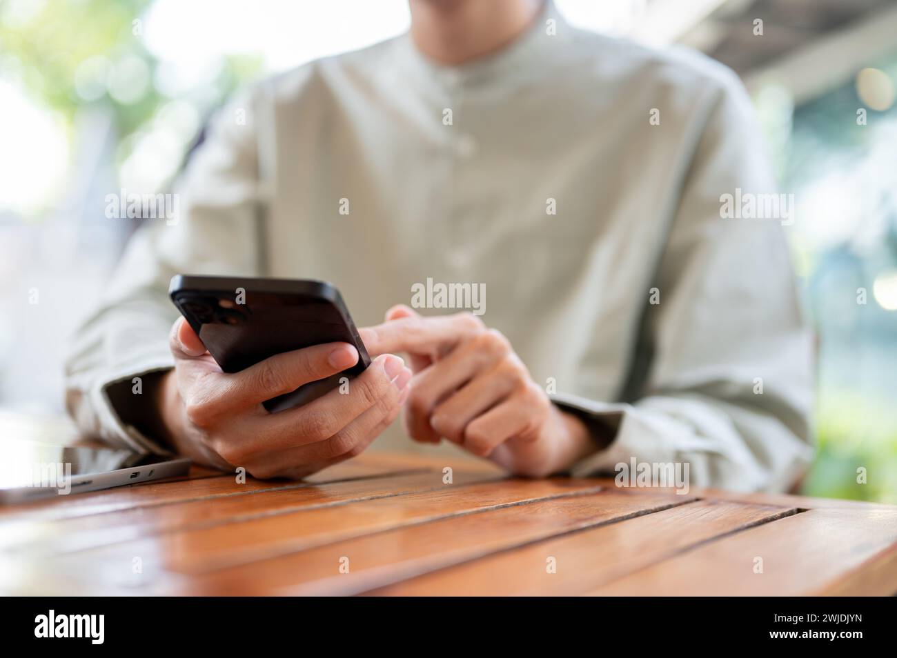 Un primo piano di un uomo che usa il suo smartphone a un tavolo in un bar. social media, invio di messaggi, controllo delle e-mail, scorrimento sull'app di shopping Foto Stock