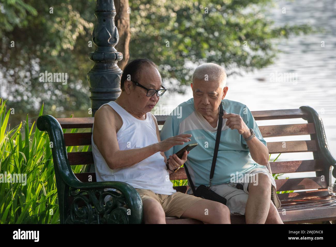 Due uomini seduti a parlare al lago Hoan Kiem ad Hanoi, Vietnam Foto Stock