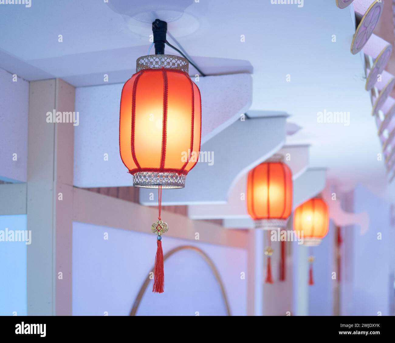 Una fila di lanterne di carta arancione appese al soffitto. Le lanterne sono rotonde e hanno un design tradizionale cinese. Sono illuminati dall'interno, Foto Stock