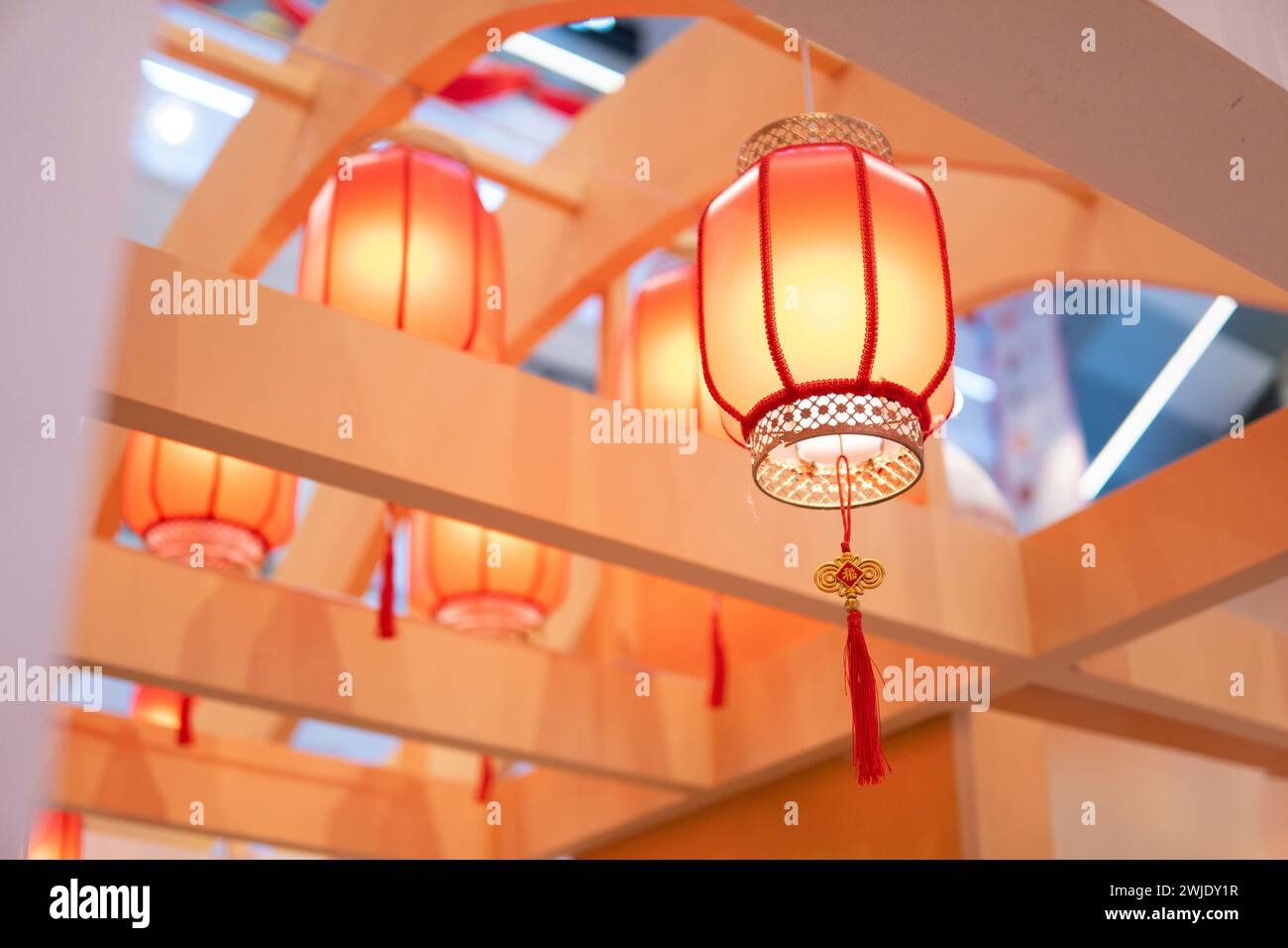 Una fila di lanterne di carta arancione appese al soffitto. Le lanterne sono rotonde e hanno un design tradizionale cinese. Sono illuminati dall'interno, Foto Stock