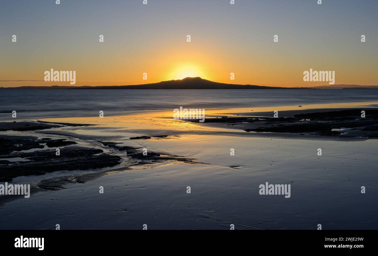 Bagliore dorato sulla cresta dell'isola di Rangitoto mentre il sole sorge. Milford Beach. Auckland. Foto Stock