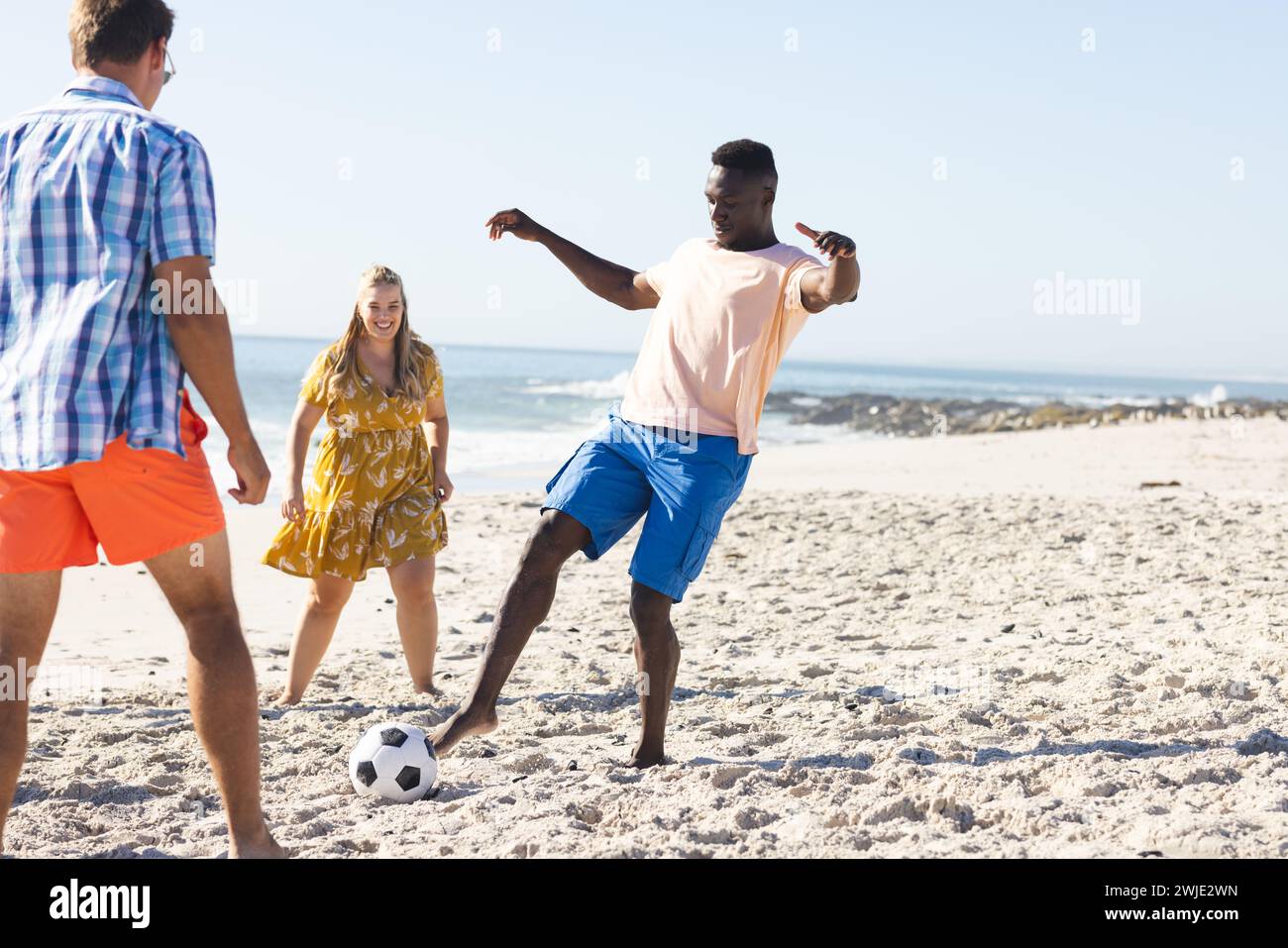 Amici eterogenei si godono una partita informale di calcio sulla spiaggia Foto Stock